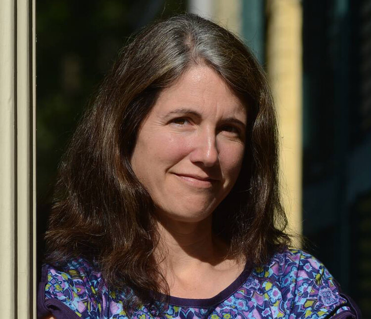 A headshot of a white woman with brown hair wearing a blue flower shirt and looking at the camera.